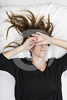 Depressed young woman is lying in her bed, covering her eyes. photo