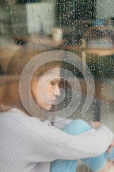 Depressed young woman near window