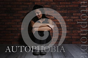 Depressed young woman sitting alone near wall. Autophobia - fear of isolation