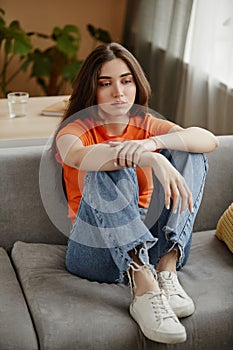 Depressed young woman sitting on couch alone staring blankly