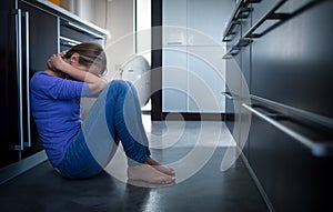 Depressed young woman, sitting on the kitchen floor