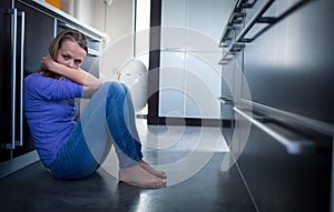 Depressed young woman, sitting on the kitchen floor,