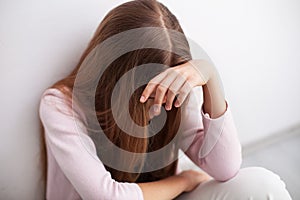 Depression in adolescence - young teenager girl sitting by wall