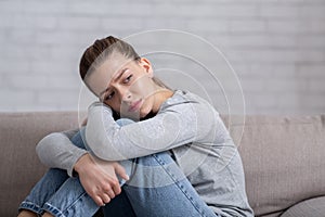 Depression and anxiety concept. Young sad woman sitting on sofa and hugging her knees, copy space