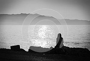 Depression. black and white photo of melancholic alone girl sitting by the sea feeling sad and contemplating