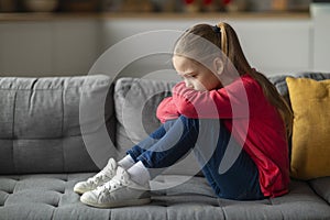 Depression In Children. Upset Little Girl Sitting On Couch At Home