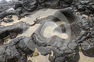 Depressions in a rock with white sand at the bottom, flooded with sea water. Small ponds excavated in lava bed on Indian Ocean