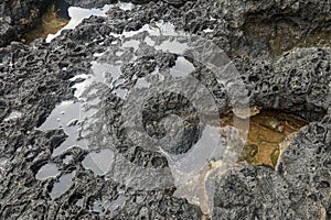 Depressions in a rock with white sand at the bottom, flooded with sea water. Small ponds excavated in lava bed on Indian Ocean