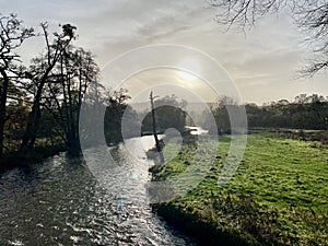 Derbyshire river with sun burning through clouds. Green grass and trees.