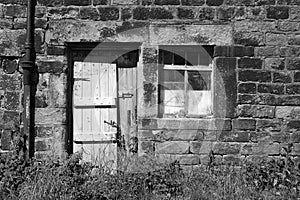 Derelict abandoned old stone house with broken window and shabby wooden door overgrown with weeds