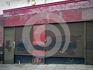 Derelict abandoned store with shuttered vandalized shop front with peeling red paint on an urban street photo