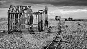 Derelict fishing hut and rails on shingle beach during stormy Wi