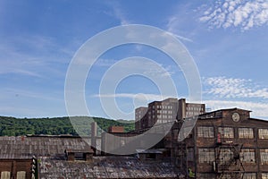 Derelict industrial warehouse with modern commercial building and forested hillside beyond