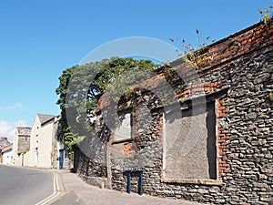 Derelict old stone building with blocked up windows, weeds growing from the roof and a street sign in brewery street in ulverston