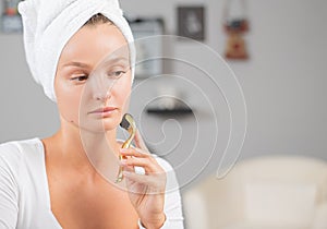 Beautiful woman is using anti aging derma roller. Woman is making needles procedure on face using meso roller photo