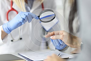 Dermatologist doctor looking at patients skin on hands using magnifying glass in clinic closeup