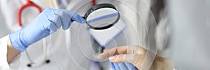 Dermatologist doctor looking at patients skin on hands using magnifying glass in clinic closeup