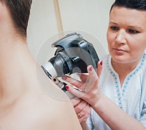 Dermatologist examines patient birthmark with dermatoscope and camera.