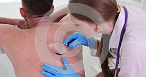 Dermatologist examines patient mole using magnifying glass in clinic