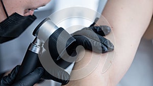A dermatologist examines a patient's mole through a dermatoscope.
