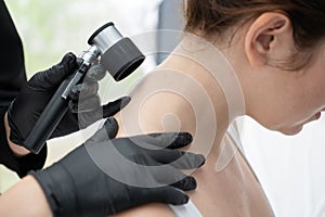 A dermatologist examines a patient& x27;s mole through a dermatoscope.