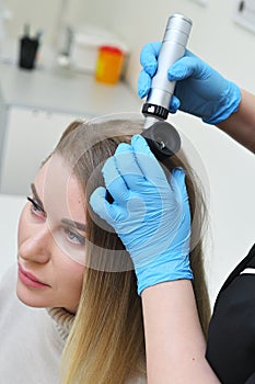 dermatologist holds a dermatoscope in his hands and examines the structure of a young woman& x27;s hair. Trichoscopy is