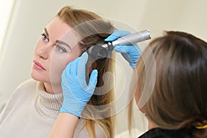 dermatologist holds a dermatoscope in his hands and examines the structure of a young woman& x27;s hair. Trichoscopy is