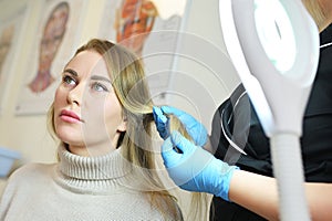 dermatologist trichologist examines the hair structure of a young woman& x27;s patient using an optical dermatoscope