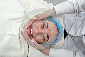 dermatologist wearing a medical mask and rubber gloves applies a mask to a client& x27;s face.