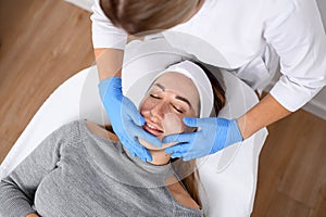 Dermatologist in white clothes and blue gloves makes a facial salon procedure for a girl with acne lying on a couch