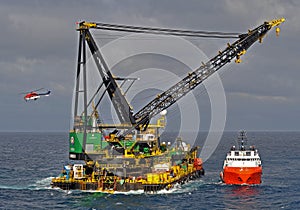 Derrick work barge offshore with departing helicopter and workboat alongside.