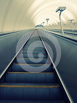 Descent into the tunnel stereo escalator stairs light from below. Modern tunnel escalator electronic system moving vintage style,