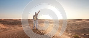 Desert adventure. Young man with backpack walking on sand dune. Dubai, United Arab Emirates