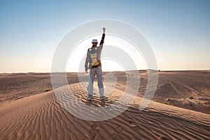 Desert adventure. Young man with backpack walking on sand dune. Dubai, United Arab Emirates