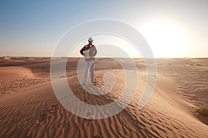 Desert adventure. Young man with backpack walking on sand dune. Dubai, United Arab Emirates