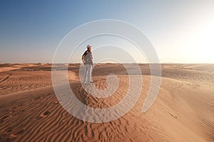 Desert adventure. Young man with backpack walking on sand dune. Dubai, United Arab Emirates