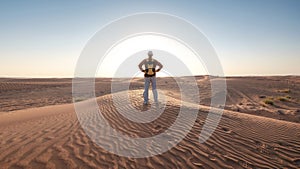 Desert adventure. Young man with backpack walking on sand dune. Dubai, United Arab Emirates