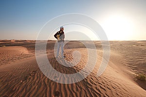Desert adventure. Young man with backpack walking on sand dune. Dubai, United Arab Emirates