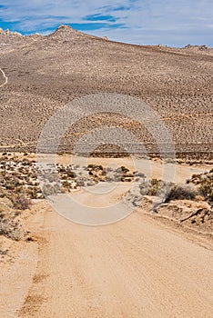 Desert dirt road curving towards mountain under a blue sky with white clouds