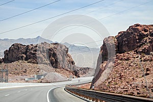 Desert highway turning right next to Hoover dam with cliffs on each side