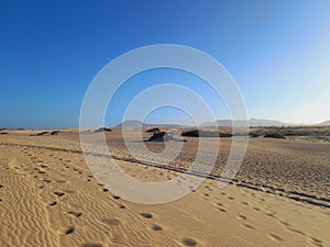 Desert landscape and dunes with footprints in the sand under blue sky and volcanoes on the horizon. Nature and extreme sports