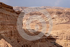 Desert landscape with sandy hills and high cliff above dry riverbed.