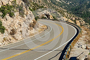 Desert mountain road in the cliffs of arizona with metal gaurd rail and yellow and white paint winding up hillside photo