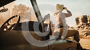 Desert Road Trip: Beautiful Female Traveler Looking Into Binoculars while Sitting on a Hood of Her