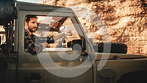 Desert Road Trip: Portrait of Handsome Male Explorer Looking out of Car Driver Window and Smiling
