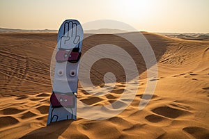 Desert safari tour in UAE. Snowboard used for sand boarding standing inserted in sand dune