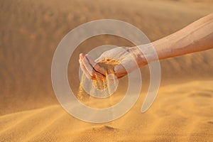 Desert, sand puffs through the fingers of a mans hand