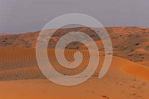 Desert at sunrise brings out bold burnt orange colored sand making a great desert landscape on rippling or rolling hills in Ras al