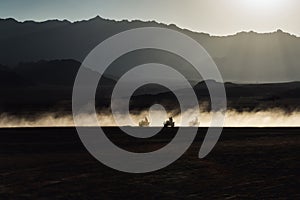 Desert at sunset. Silhouettes of people moving on buggy car in a cloud of dust and sand. Travel concept.