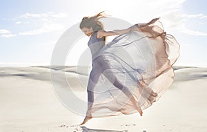 Desert, woman and fashion with dress, jumping and relaxing with confidence and getaway trip. Person, outdoor and sand